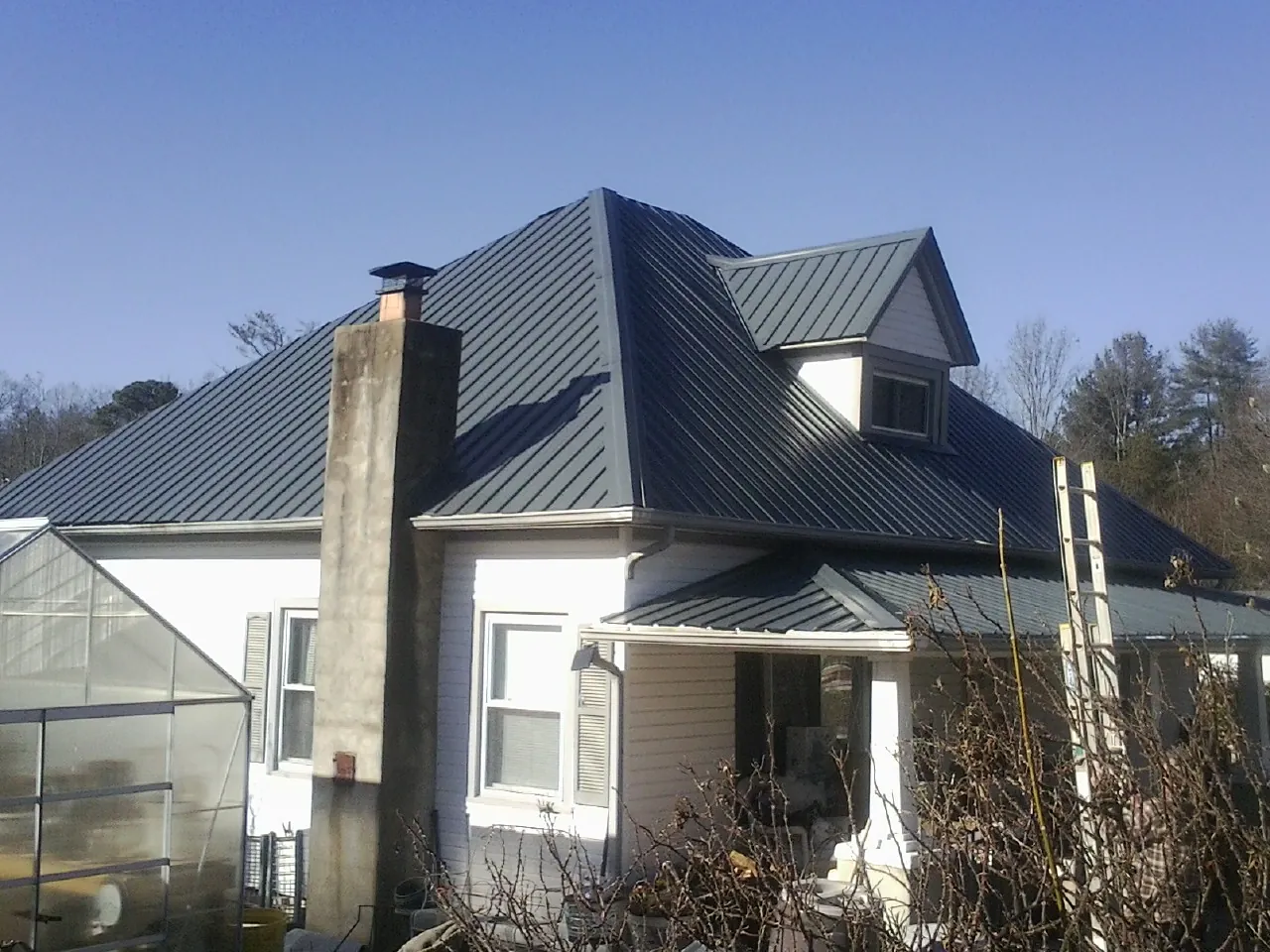 Dark blue standing seam metal roof on a white farmhouse with dormer — Slate & Tile Roof Repair by Roofing Brothers in Bairdford