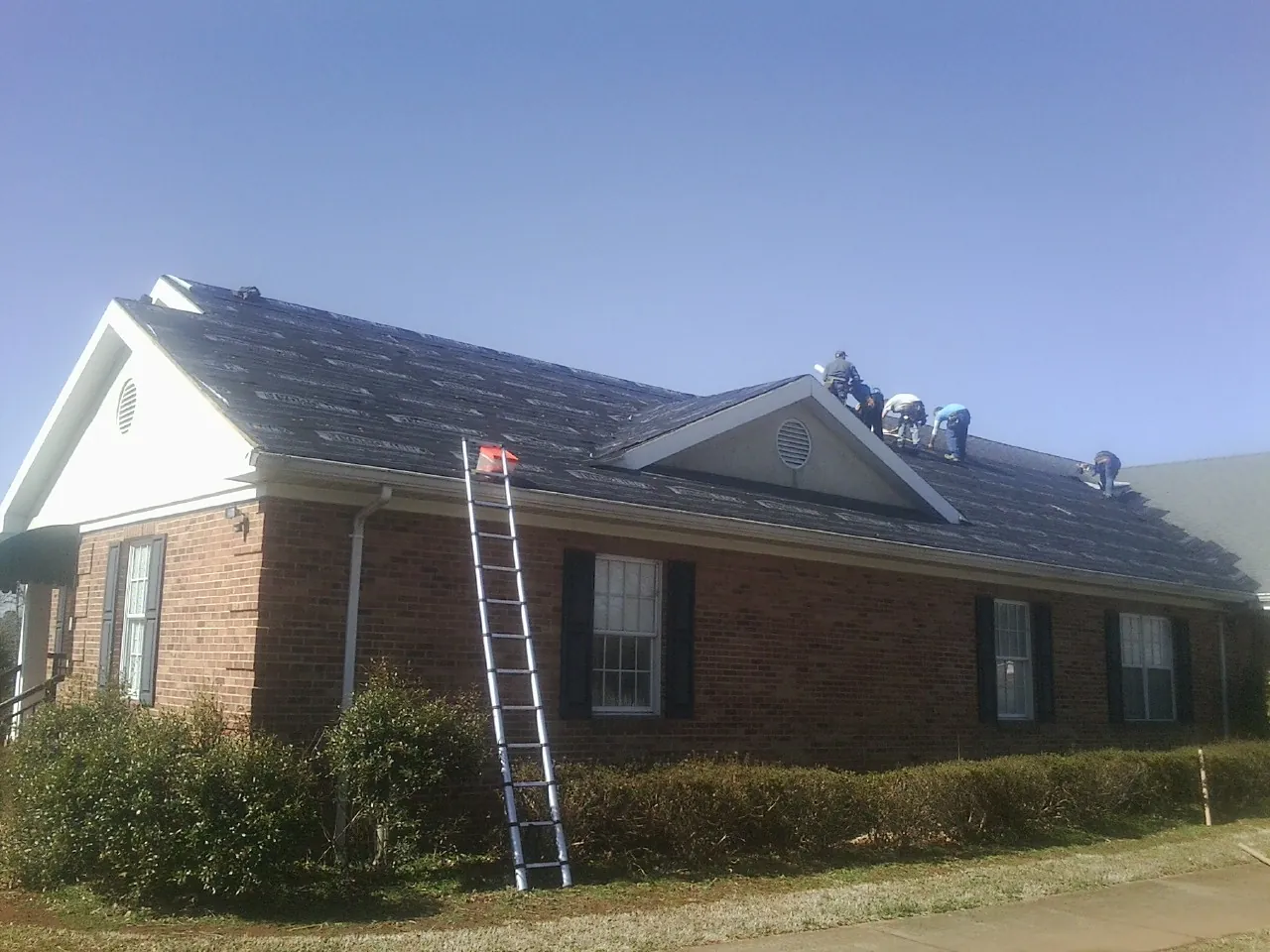 Crew tearing shingles off a brick ranch roof with a ladder set — Metal Roof Repair work by our crew in Bairdford