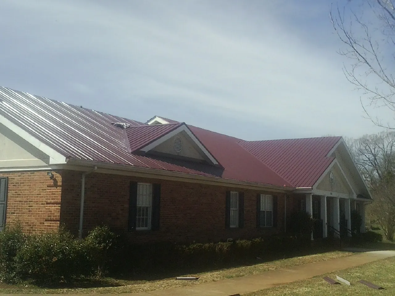 Red metal roof with gabled entries on a long brick building, from a Hail Damage Roof Repair job in Bairdford