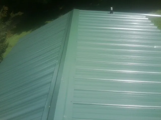 New green metal panels meeting at the ridge of a roof — Flat Roof Repair work by our crew in Bairdford