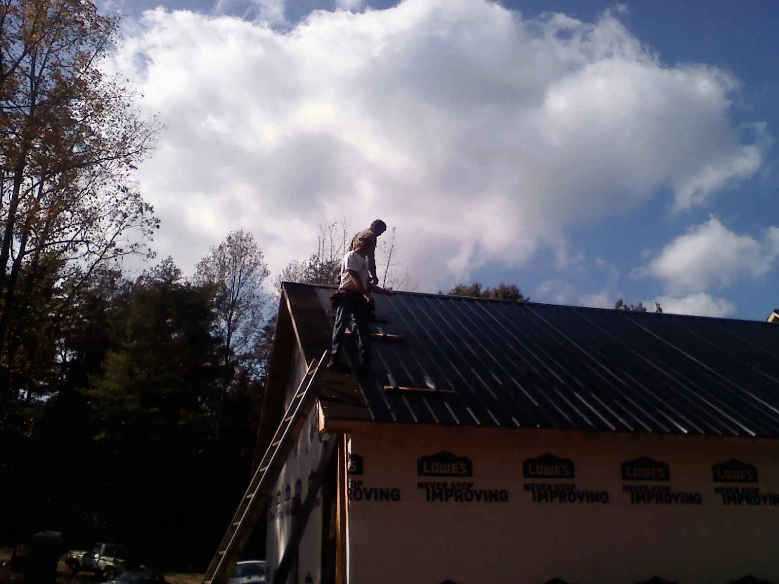 Roofer fastening dark metal panels high against a cloudy sky, from a Roof Inspection job in Bairdford