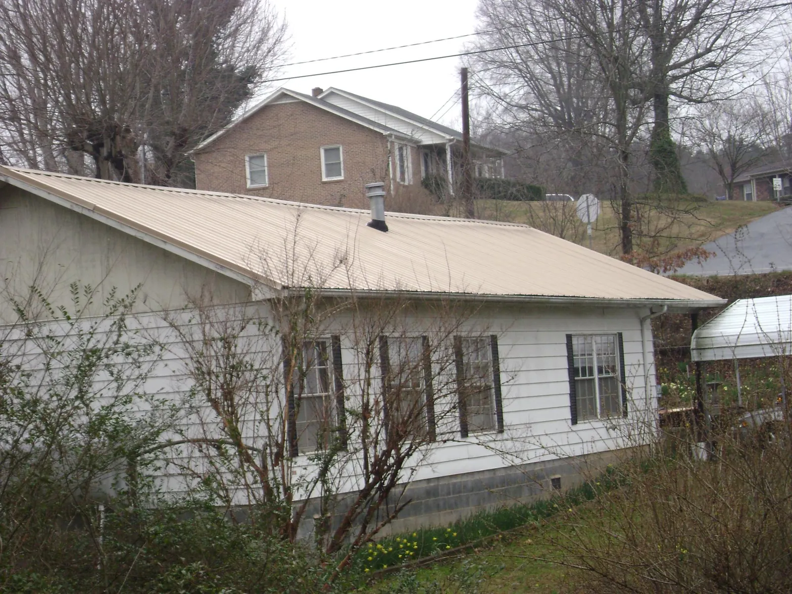 Tan metal roof on a white sided house set into a hillside — Commercial Roofing by Roofing Brothers in Bairdford