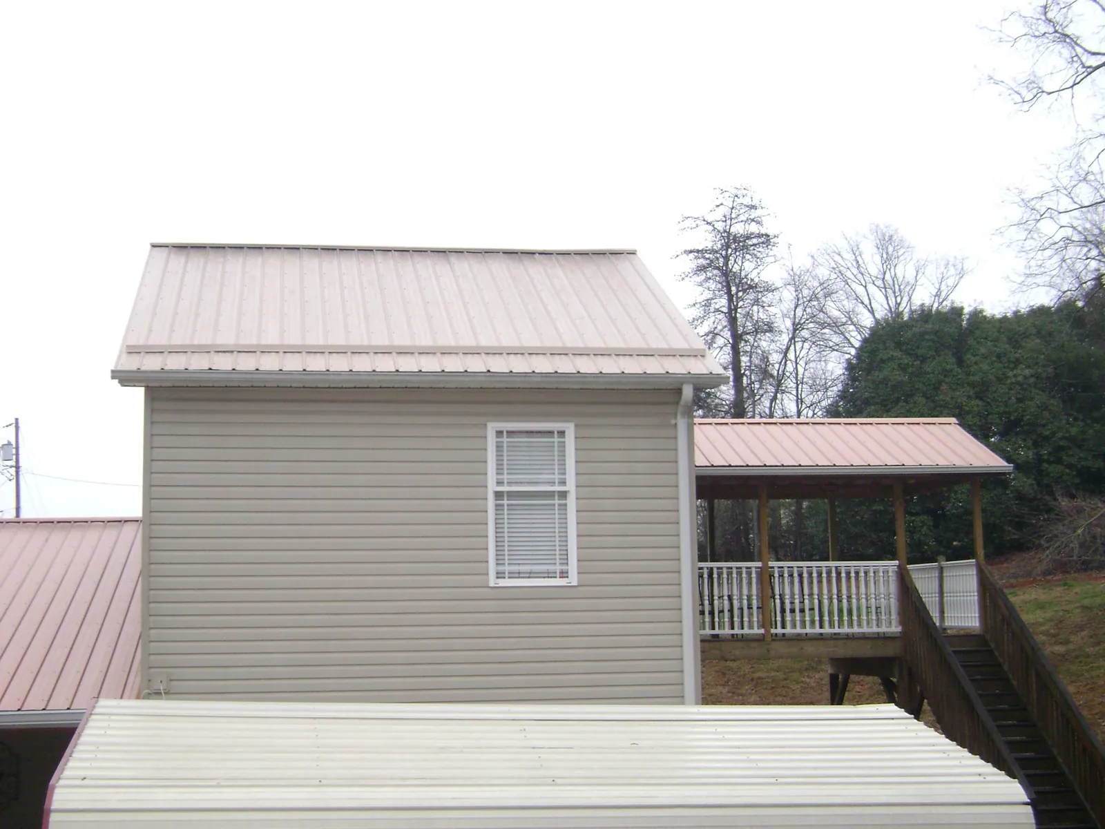 Tan metal roofs on a two story addition and attached porch, from a Roof Replacement job in Bairdford